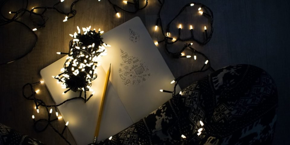 A notebook surrounded by Christmas lights on the floor in front of a person’s legs