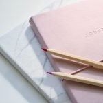 Pink and marble journals with red and purple coloring pencils sitting on top of them